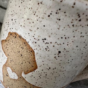 Pode incluir: Uma caneca de cer&acirc;mica com esmalte esbranqui&ccedil;ado salpicado, apresentando uma silhueta de c&atilde;o lisa e sem esmalte na cor castanho-claro na lateral. A silhueta do c&atilde;o cont&eacute;m um pequeno recorte branco em forma de cora&ccedil;&atilde;o. Caneca curva e brilhante.