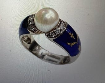 Puede incluir: Un anillo de plata con una gran perla redonda en el centro. El anillo presenta una banda de esmalte azul con detalles florales dorados y una fila de pequeños diamantes. El diseño del anillo es elegante y detallado.