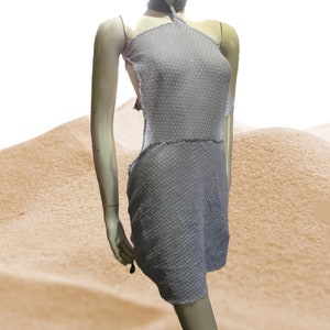 Könnte beinhalten: Ein graues Halstuchkleid mit strukturiertem Stoff und einem Ausschnitt an den Seiten. Das Kleid wird auf einer Schaufensterpuppe vor einem sandfarbenen Hintergrund gezeigt.