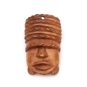 May include: A light brown carved wooden pendant shaped like a human face. The carving features a textured, rope-like pattern across the forehead and a small circular hole at the top for suspension. The facial features include a nose and lips.