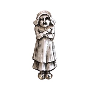 May include: A silver-toned figurine of a young girl wearing a bonnet and a long dress. The girl's arms are crossed, and the figure has a detailed, antique appearance. The figurine is standing upright against a white background.