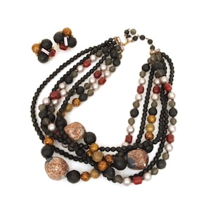 May include: A multi-strand necklace and matching earrings set. The necklace features black, red, gold, and pearl-colored beads, with large, textured, brown stones. The earrings have a cluster design with black and gold accents.