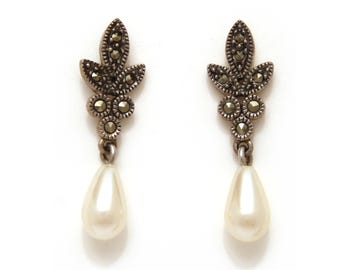 May include: A pair of silver dangle earrings with a pearlescent teardrop charm and a cluster of marcasite stones in a floral design.