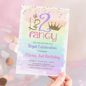 May include: A colorful invitation for a child's birthday party. The invitation features a watercolor background with a rainbow gradient and a gold crown. The text on the invitation reads "Turn 2 Fancy" and "Olivia's 2nd Birthday".