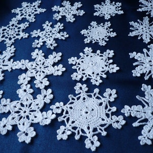Op de afbeelding: Een verzameling witte gehaakte sneeuwvlokornamenten met ingewikkelde, kantachtige patronen met zesvoudige radiale symmetrie. Elk afzonderlijk stuk toont delicaat draadwerk met gevarieerde geometrische ontwerpen en opengewerkte details.