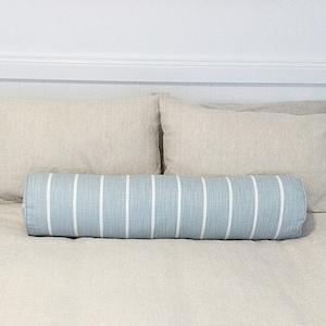 May include: A bed with white linen bedding and two beige pillows. A blue and white striped bolster pillow is placed in the center of the bed.