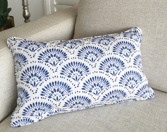 May include: A rectangular decorative pillow with a white background and a blue fan-shaped pattern. The pillow is placed on a beige sofa, offering a pop of color and pattern to the neutral setting. The pillow's design adds a touch of elegance.