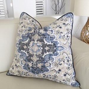 May include: A decorative cushion with a blue and grey patterned design. The cushion has a navy blue trim and is made of a soft, textured fabric.