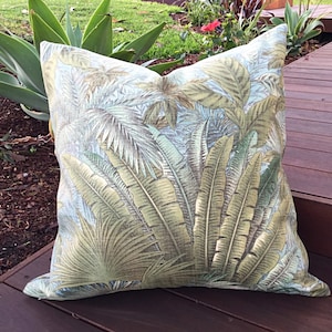 May include: A green and brown tropical leaf patterned throw pillow. The pillow is on a wooden deck.