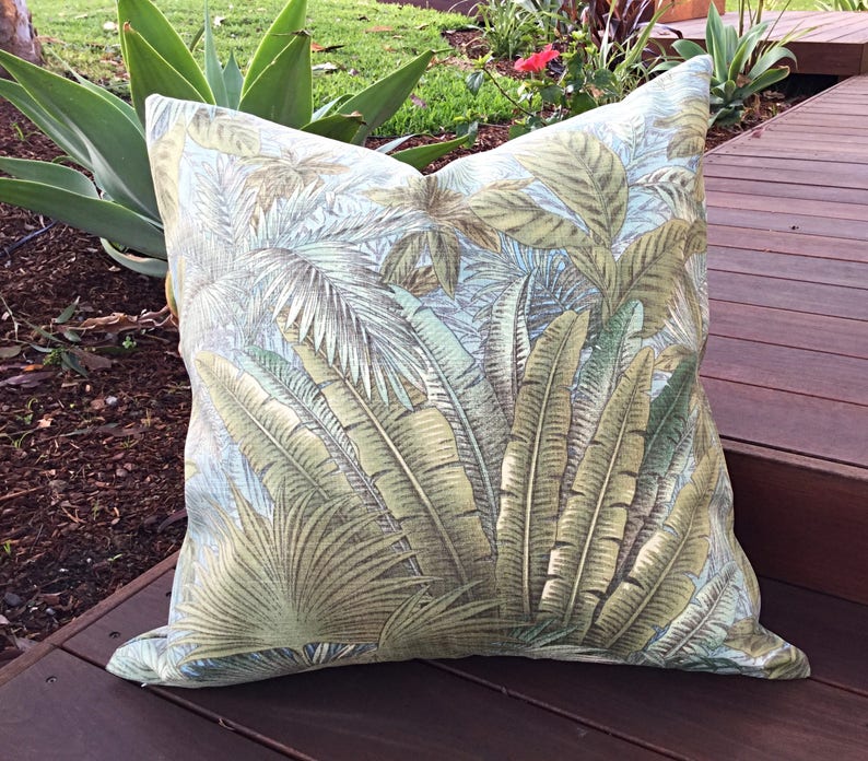 May include: A green and brown tropical leaf patterned throw pillow. The pillow is on a wooden deck.