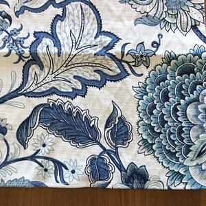 Op de afbeelding: Close-up van een stof met een bloemenpatroon in blauw- en wittinten. Het ontwerp toont grote, gestileerde bloemen en bladeren, wat een botanisch thema cre&euml;ert. De stof heeft een linnenachtige textuur.