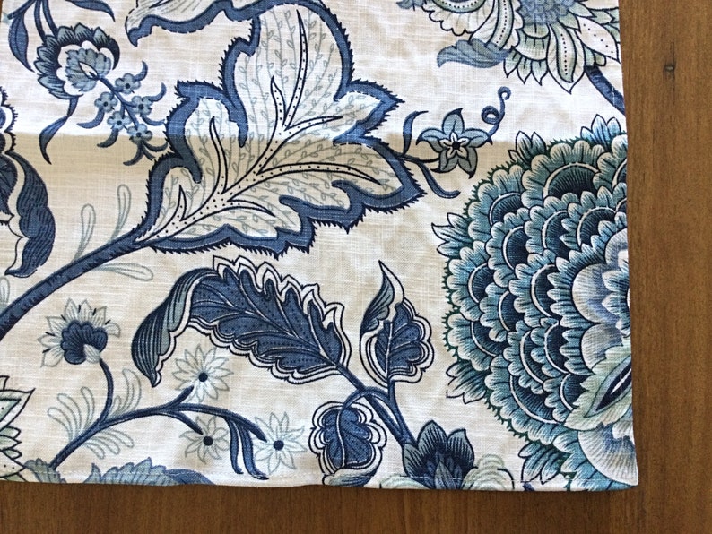 Op de afbeelding: Close-up van een stof met een bloemenpatroon in blauw- en wittinten. Het ontwerp toont grote, gestileerde bloemen en bladeren, wat een botanisch thema cre&euml;ert. De stof heeft een linnenachtige textuur.