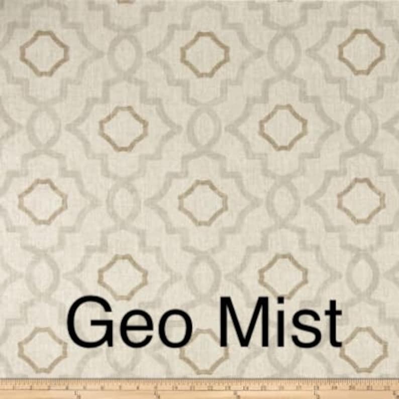 May include: Cream-colored fabric with a geometric pattern in light gray and tan. The design features interlocking shapes and the text "Geo Mist" in black. A wooden ruler is at the bottom.