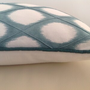 May include: A white and teal blue pillow with a geometric pattern. The pillow has a teal blue zipper and a teal blue trim.