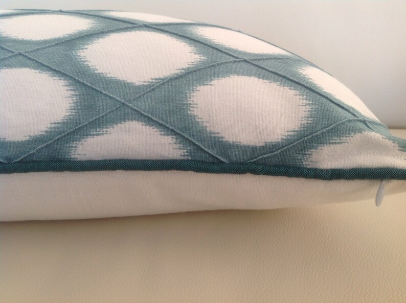 May include: A white and teal blue pillow with a geometric pattern. The pillow has a teal blue zipper and a teal blue trim.