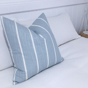 May include: A blue and white striped throw pillow with a textured fabric. The pillow is on a white bed with a white headboard.