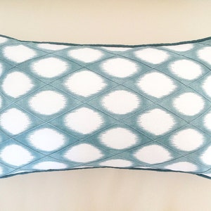 May include: A teal and white patterned throw pillow with a diamond-shaped design. The pillow has a teal border.