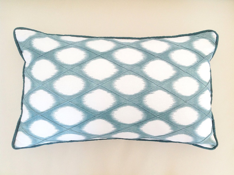 May include: A teal and white patterned throw pillow with a diamond-shaped design. The pillow has a teal border.