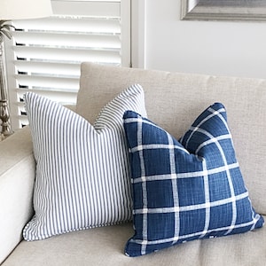 May include: Two decorative throw pillows on a beige couch. One pillow has a blue and white striped pattern, and the other has a blue and white plaid pattern.
