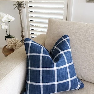 May include: A blue and white plaid throw pillow on a beige couch. The pillow is made of a soft, textured fabric.