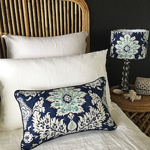 May include: A bedroom scene featuring a decorative pillow with a blue and white floral pattern, a matching lampshade, and white bedding. The headboard is made of woven rattan.