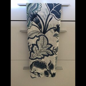 Op de afbeelding: Een decoratieve keukendoek met een bloemenpatroon in blauw- en wittinten. De doek hangt aan een kastdeur. Het bloemmotief toont grote bladeren en bloemen.