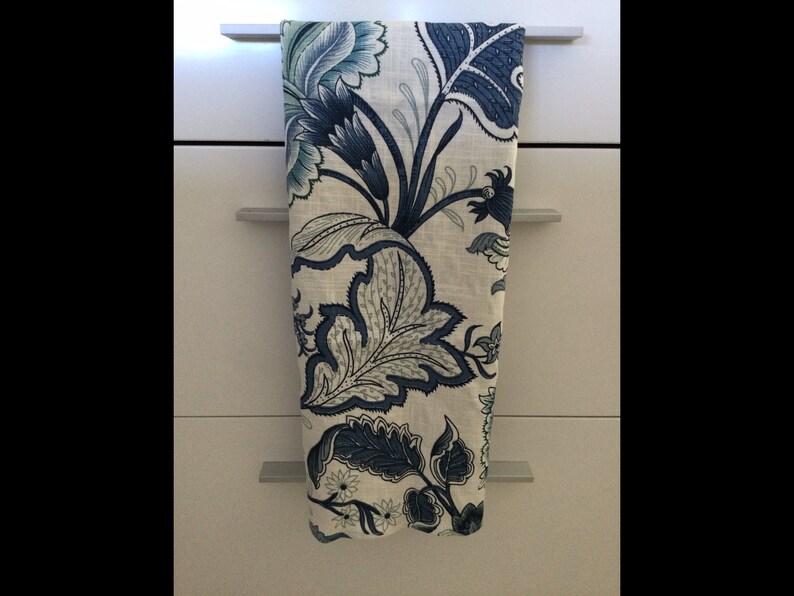 Op de afbeelding: Een decoratieve keukendoek met een bloemenpatroon in blauw- en wittinten. De doek hangt aan een kastdeur. Het bloemmotief toont grote bladeren en bloemen.