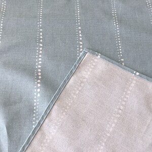 May include: A light blue table runner with a white dotted pattern. The runner is reversible, with a solid light gray color on the other side.