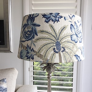 May include: A white lampshade with a blue and green floral pattern featuring palm trees and flowers. The lampshade is on a silver lamp base with a pineapple finial.