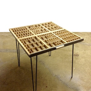 May include: A wooden table with a drawer that has a grid of compartments. The table has four black hairpin legs.