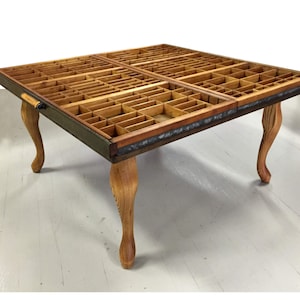 May include: A square wooden coffee table with a unique top made from repurposed printer's trays. The table has four turned wooden legs.
