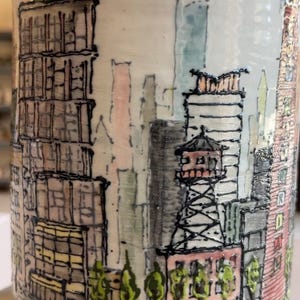 May include: A set of three ceramic mugs with a speckled, matte finish. The mugs are in shades of cream, light brown, and dark brown. Each mug has a simple, minimalist design and a rounded handle.