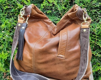 May include: A brown leather shoulder bag with a wide, dark brown strap featuring white stitching. The bag has gold-colored hardware and a dark brown tassel. The bag is made of soft leather and has a slouchy design.
