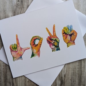 May include: A greeting card with the word "LOVE" spelled out in American Sign Language. The hands are painted in vibrant colors, including red, orange, yellow, green, blue, and purple.