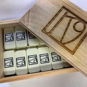 May include: A wooden box with a lid containing a set of white dominoes with black abstract designs. The lid has a carved design of the same abstract design.