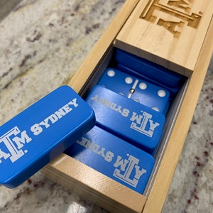 May include: A wooden box with a blue and white domino set inside. The dominoes are labeled with the text "A.M. SYDNEY".