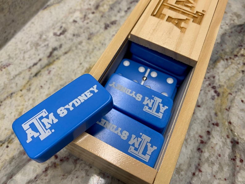 May include: A wooden box with a blue and white domino set inside. The dominoes are labeled with the text "A.M. SYDNEY".