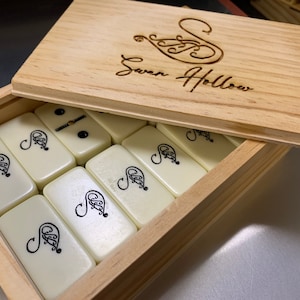May include: A wooden box with a hinged lid, the lid is open and shows the inscription "Swan Hollow". The box contains a set of white dominoes with black markings.
