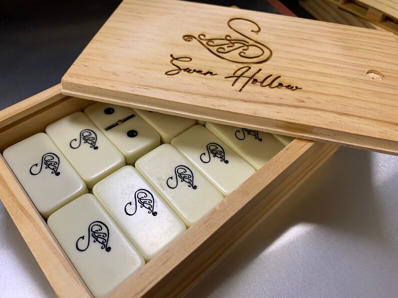 May include: A wooden box with a hinged lid, the lid is open and shows the inscription "Swan Hollow". The box contains a set of white dominoes with black markings.