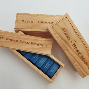 May include: Three wooden boxes with engraved names and titles: "David - Groom", "Reverend Greg Pickup", and "Aldo - Best Man". The boxes are stacked on top of each other and contain blue dominoes.