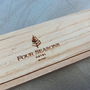 May include: A wooden box with the Four Seasons Hotel Miami logo engraved on the top. The logo features a stylized tree and the text "Four Seasons Hotel Miami".