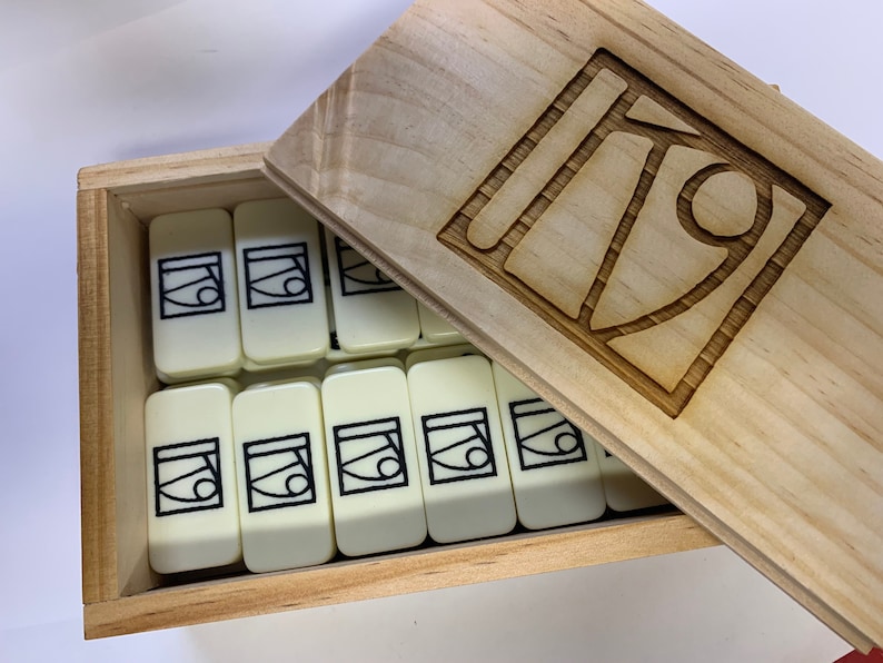 May include: A wooden box with a lid containing a set of white dominoes with black abstract designs. The lid has a carved design of the same abstract design.