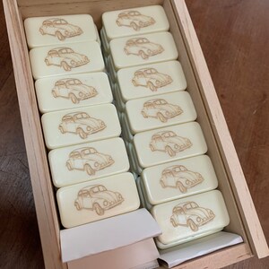May include: A wooden box filled with white dominoes featuring a vintage car design. The dominoes are arranged in rows and are ready for a game.