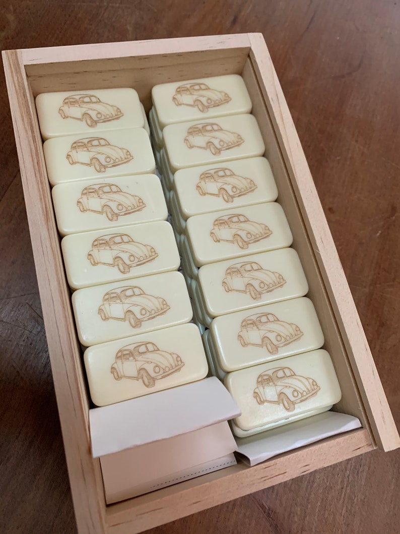 May include: A wooden box filled with white dominoes featuring a vintage car design. The dominoes are arranged in rows and are ready for a game.