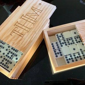 May include: A wooden box with the word "TIME" engraved on the lid. The box contains a set of white dominoes with black dots. The box is open and the dominoes are visible.