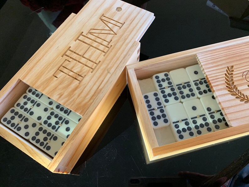 May include: A wooden box with the word "TIME" engraved on the lid. The box contains a set of white dominoes with black dots. The box is open and the dominoes are visible.