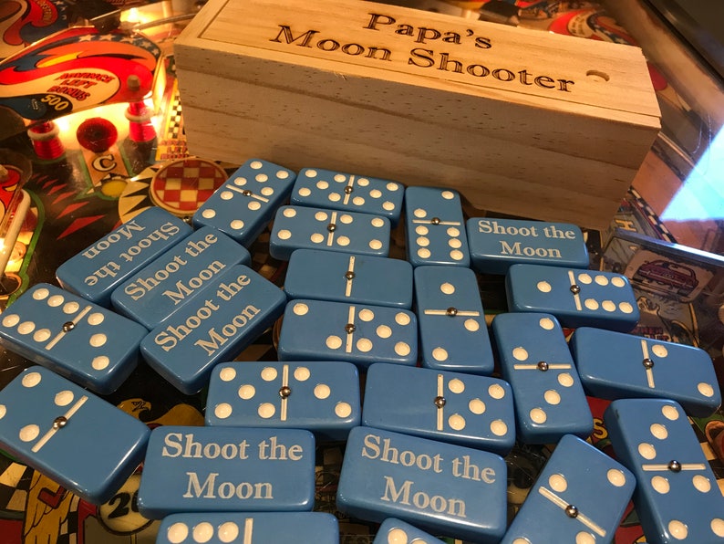 May include: A set of blue dominoes with white dots and the text "Shoot the Moon" on each tile. The dominoes are in a wooden box labeled "Papa's Moon Shooter".