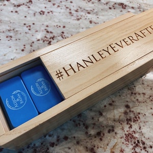 May include: A wooden box with a blue lid engraved with "#HANLEYEVERAFTER" and two blue dominoes inside. The dominoes are engraved with "ALISON & BRIAN" and a wheat design.