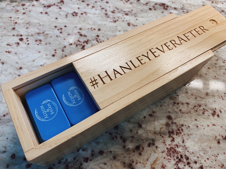 May include: A wooden box with a blue lid engraved with "#HANLEYEVERAFTER" and two blue dominoes inside. The dominoes are engraved with "ALISON & BRIAN" and a wheat design.
