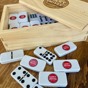 May include: A wooden box with a set of dominoes. The box is labeled "Lucky Driver Key Largo". The dominoes are white with black dots and have the same logo on them.